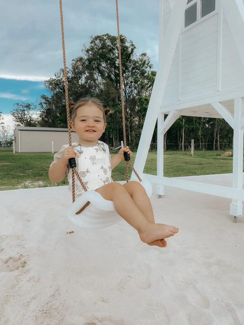 Young child on swing set, sand pit and white cubby house