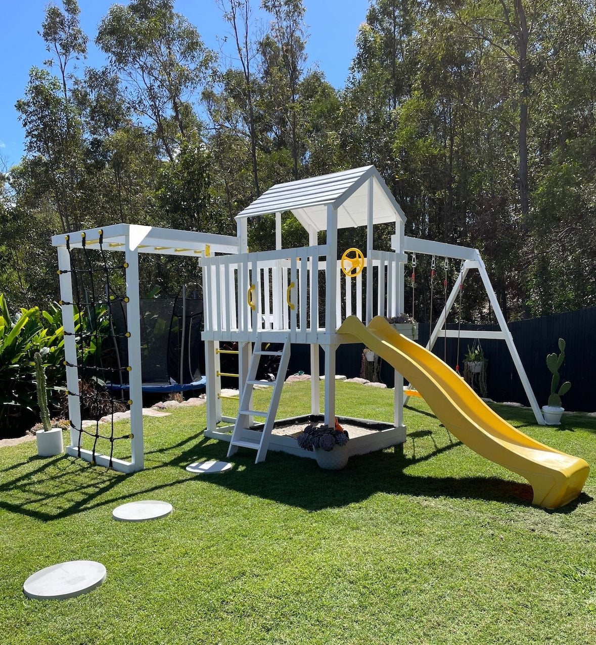 Children's playset with a yellow slide on a grassy area with trees in the background