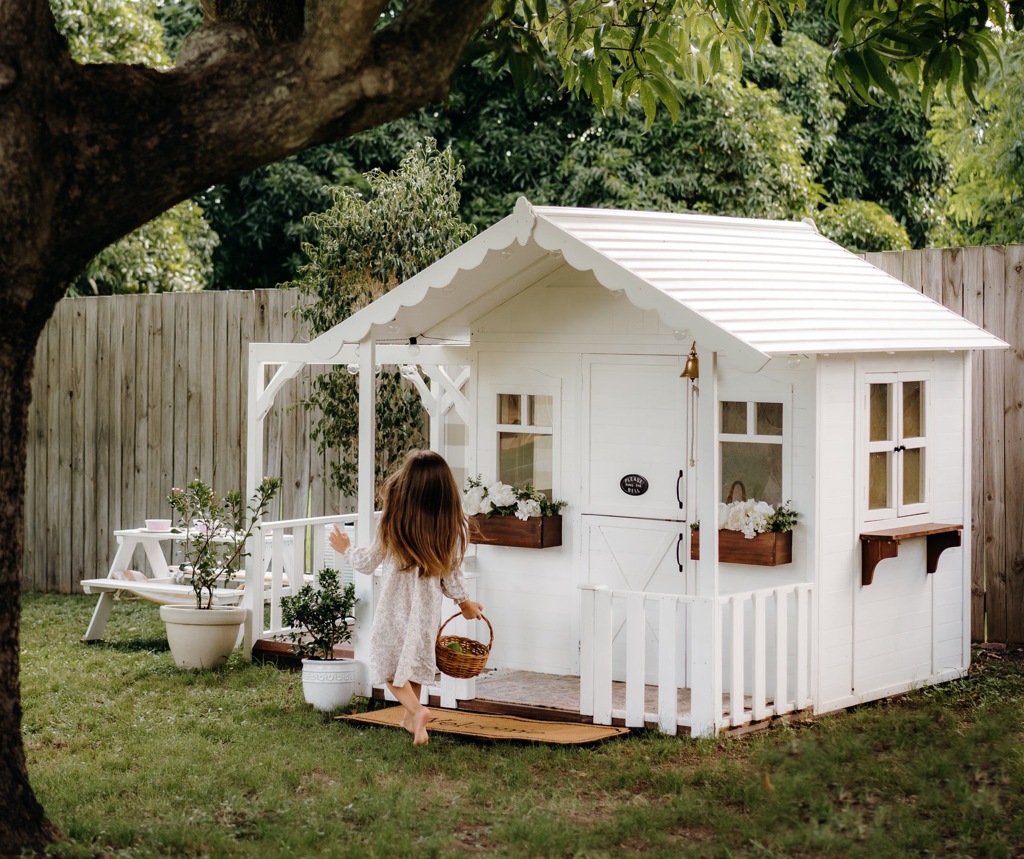 White Frankie Grand Cubby House from Hide & Seek Kids in a garden with a child sitting on the porch
