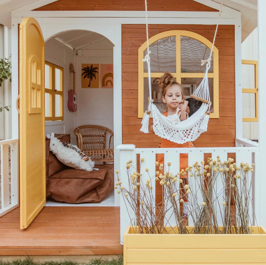 girl playing at the front of a wooden cubby house with the door open