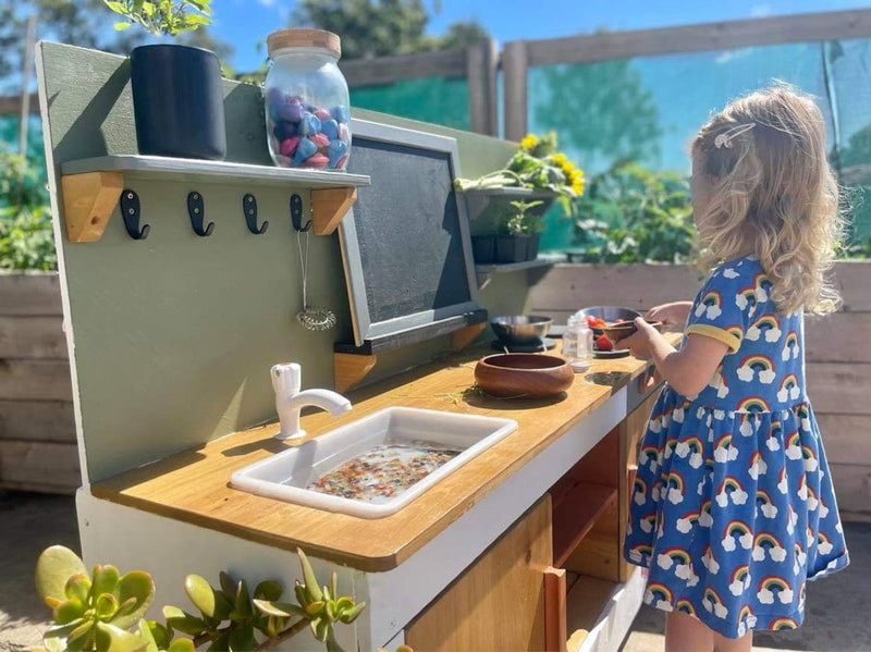 Little girl playing with a mud kitchen outside.