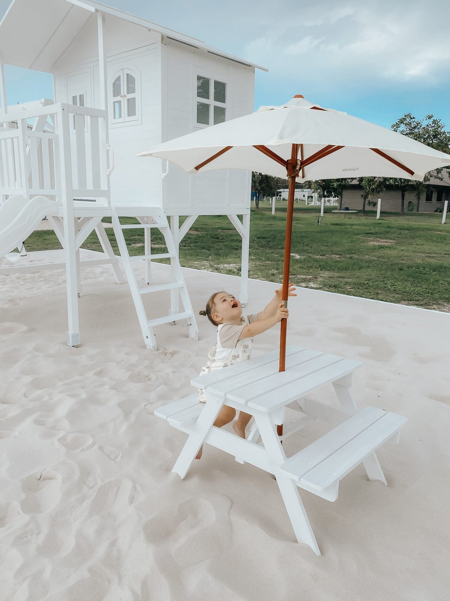 White wooden Marlie Cubby playhouse with pitched roof and window openings, designed for children's indoor or outdoor play