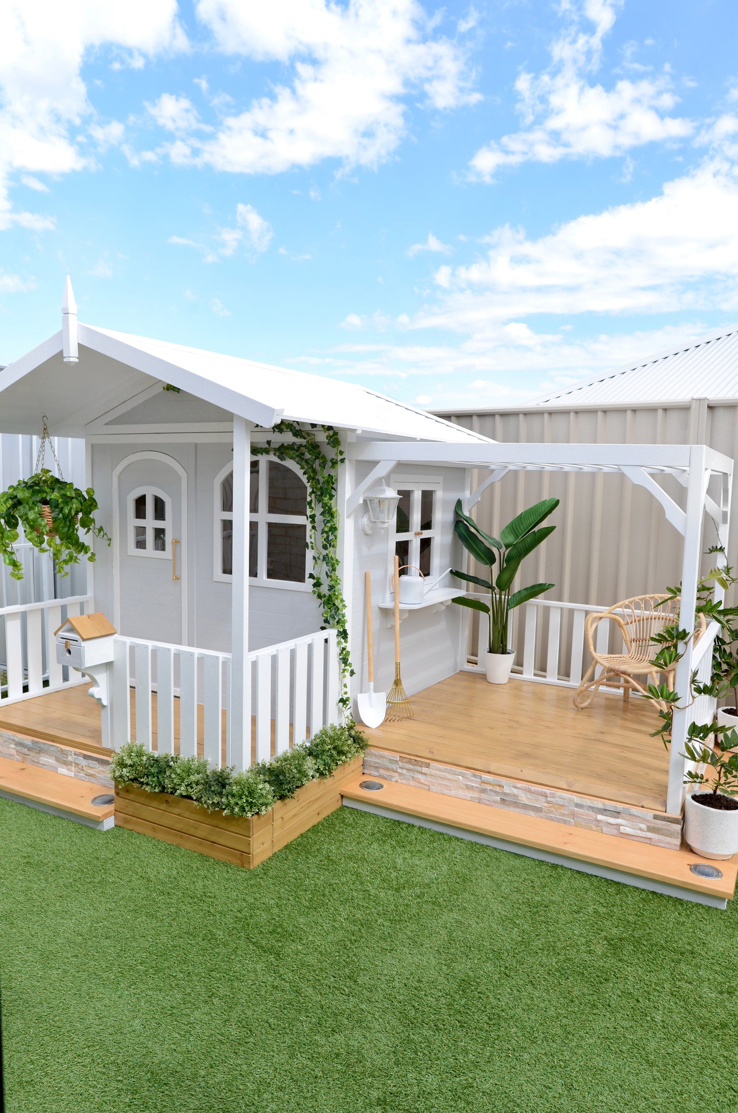 Billie Grand Cubby House by Hide & Seek Kids – grey painted timber cubby with veranda and large arched windows. The Pergola Add-on installed with the cubby house. Flower Box Add-ons surround the cubby house.