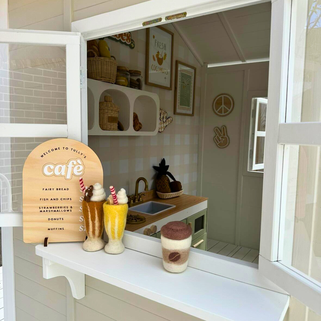 Billie Grand Cubby House by Hide & Seek Kids – opened side window with Cubby Shelf Add-on installed looking into the cubby house with a Mud Kitchen present. Accessories sitting on shelf.