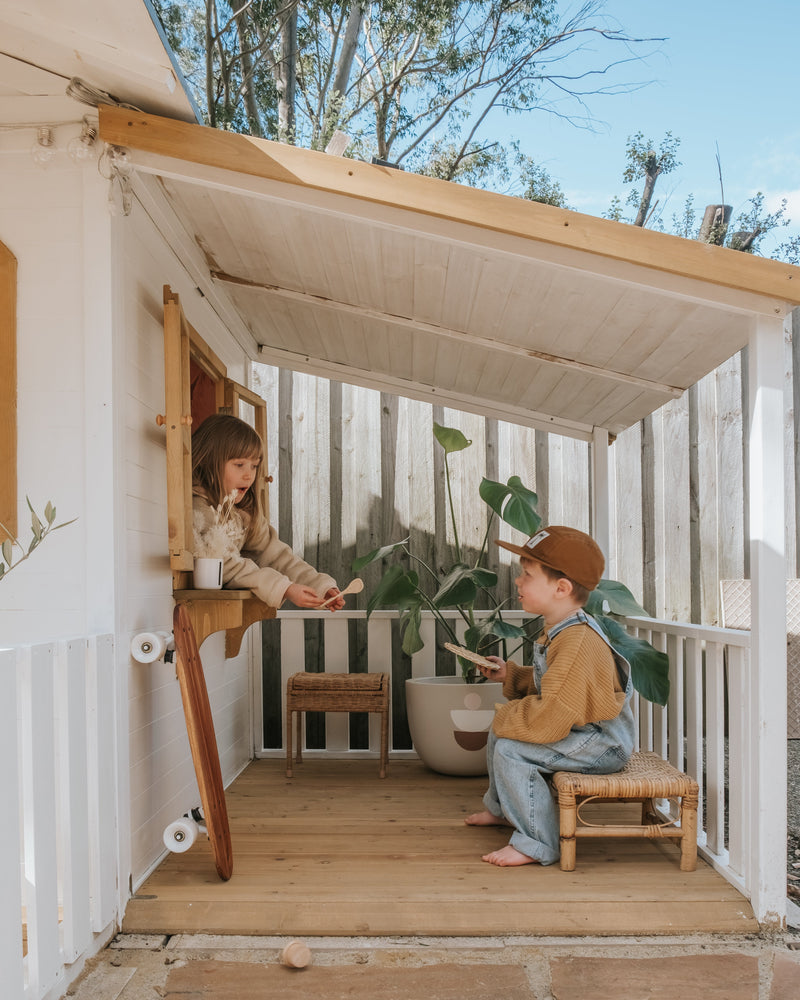 Two children playing inside a small wooden playhouse with a stone patio outside.