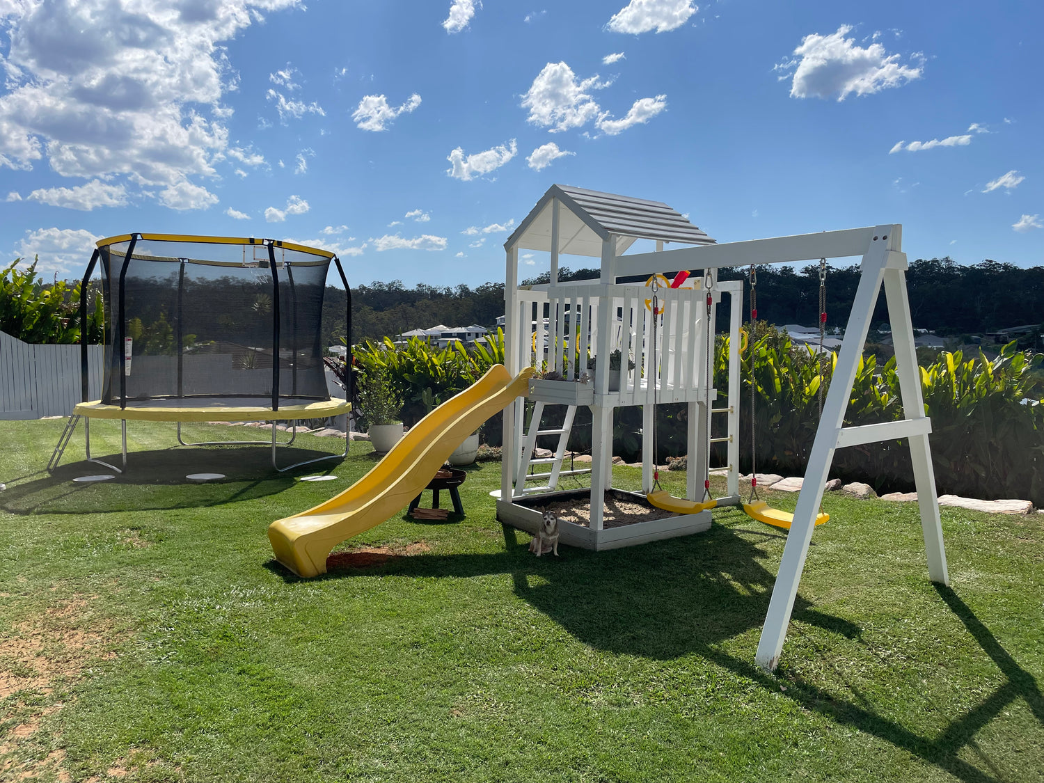 River Fort Set setup in backyard, yellow slide, swings and accessories. Painted white. Trampoline setup in background. 