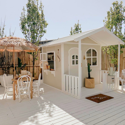 Billie Grand Cubby House by Hide & Seek Kids – Side view of white timber cubby with veranda and large arched windows. Side windows opened, with servery shelf. 