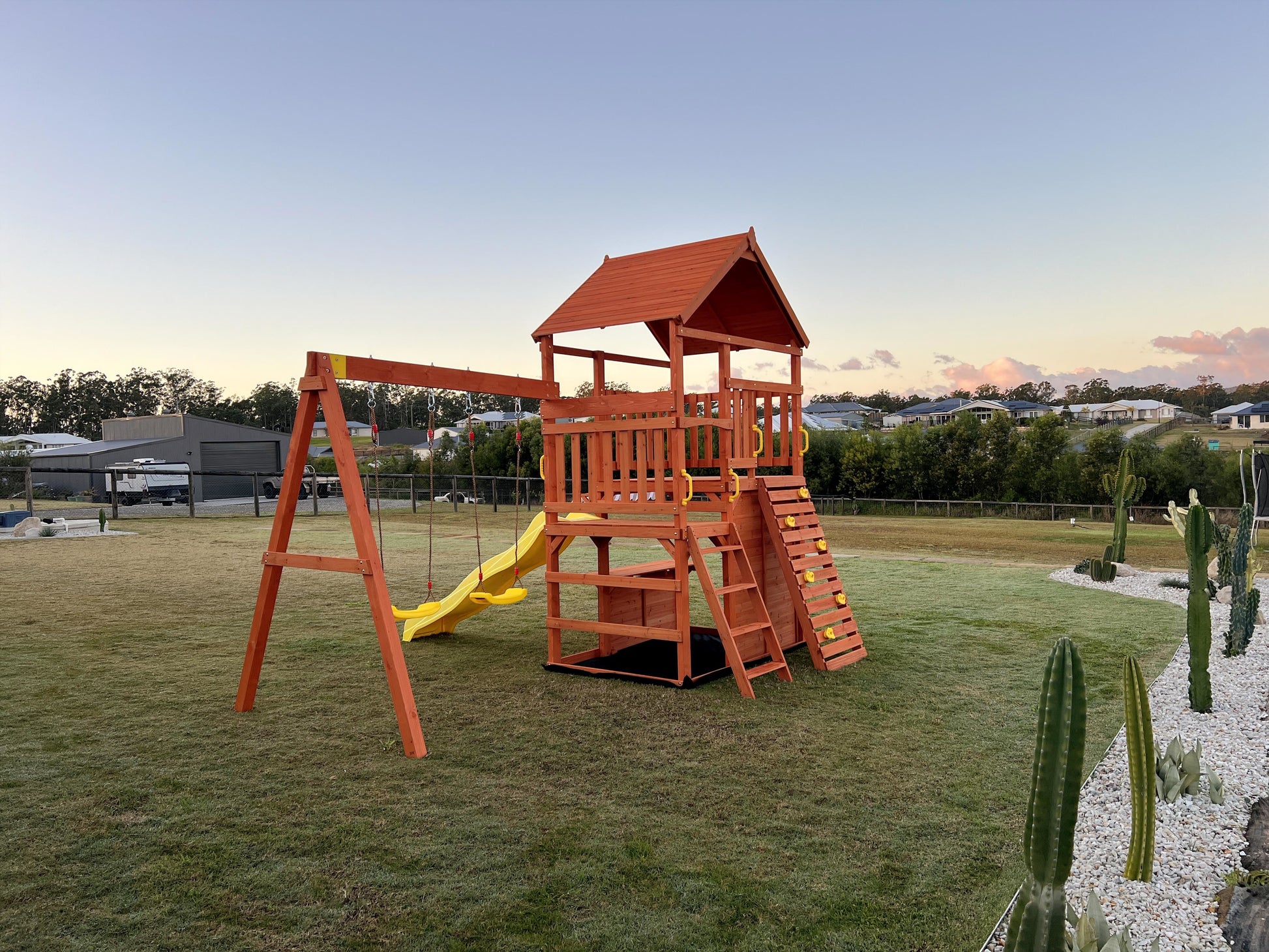 Backyard setup of The Rusty Fort including yellow slide, yellow swing seats, and timber structure. 