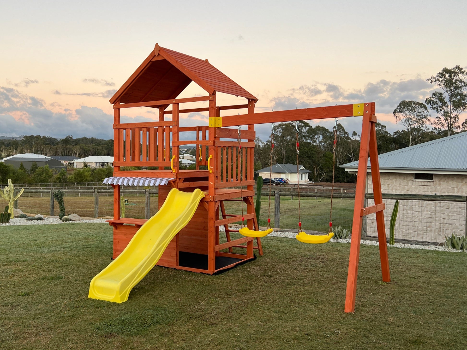 Front side view of The Rusty Fort with yellow wavy slide, double swings, and café-style front window