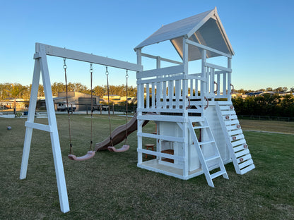 The Rusty Fort Cubby House by Hide & Seek Kids showing climbing wall, rope swings, and elevated playhouse with stairs.